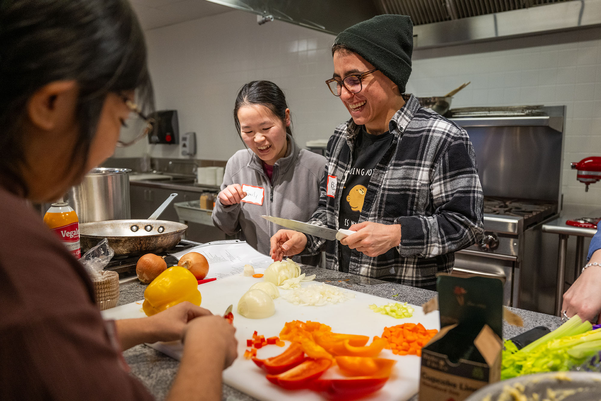 Photo: A picture of three people gathered around a cutting board and chopping onions and peppers